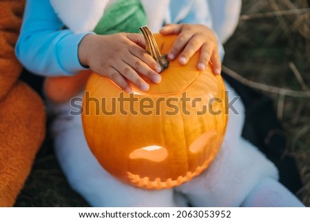 Child sitting with carved pumpkin. Small baby in white bunny costume. Halloween, trick or treat concept. Symbol of All Hallows' Eve