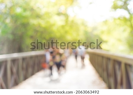 Blurred motion many people walking on wooden bridge with high fence in nature trail near Dallas, Texas, America. Lush green trees.