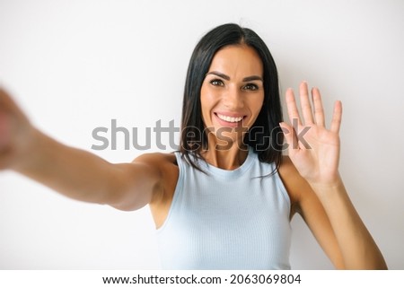 Happy young woman making selfie photo while waving palm isolated on a white background