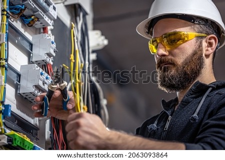 A male electrician works in a switchboard with an electrical connecting cable. Royalty-Free Stock Photo #2063093864