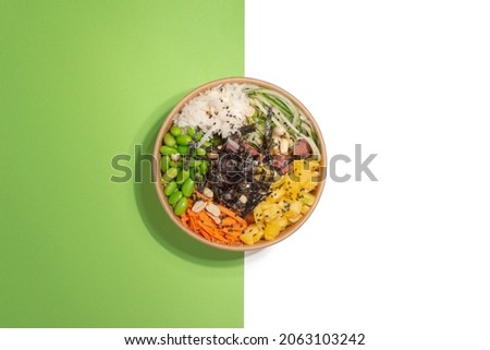 a bowl of salad poke and tuna, carrot, cucumber and pineapple on a background divided in two, green and white, healthy food, no people Royalty-Free Stock Photo #2063103242