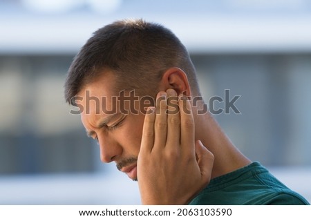 Young man with earache, otitis or tinnitus. Ear inflammation. Man suffering from ear pain Royalty-Free Stock Photo #2063103590