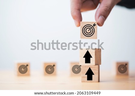 Businessman holding wooden cube block which print screen target board and lay down on up arrow block for enhance setup new challenges business objective concept.