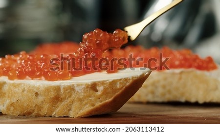 Putting red caviar on bread and butter, close-up of caviar sandwich. Salmon salted orange roe. Raw seafood. Luxury gourmet food. Delicious and tasty fish products. Russian cuisine. Royalty-Free Stock Photo #2063113412