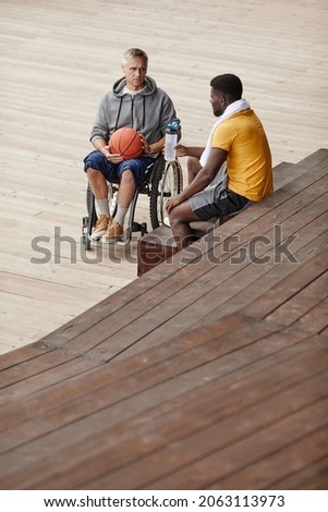African young man talking to mature man with disability while sitting outdoors