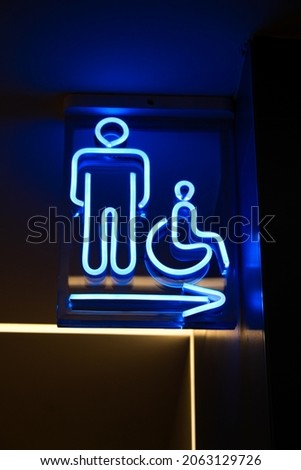 Glowing Blue outlined sign on glass for man and handicapped toilet in the shopping mall mall. WC sign with lit up arrow under it.