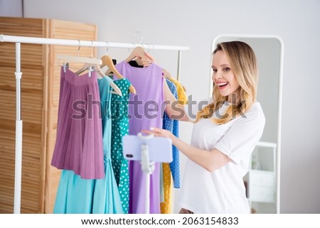 Photo portrait woman choosing dress in boutique making vlog with cellphone