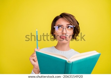Photo of smart lady read book hold pencil look empty space wear specs blue pullover isolated yellow color background