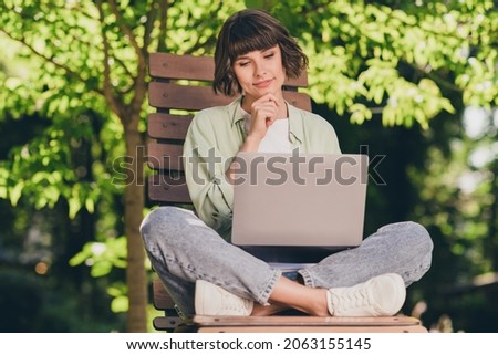 Full length body size photo smiling young girl sitting on bench working on computer thoughtful