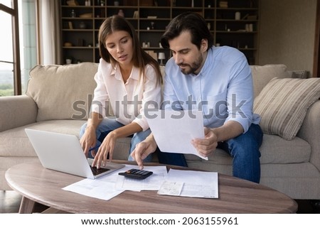 Concentrated young family couple calculating expenditures, analyzing paper bank bills, managing monthly budget, planning investment, paying for service or utilities online using computer app. Royalty-Free Stock Photo #2063155961