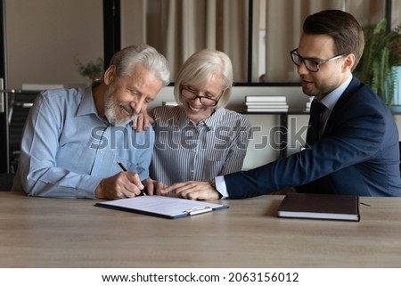 Closing deal. Happy satisfied husband wife retirees put own signatures under life insurance policy sale purchase contract at lawyer consultant office. Aged couple visit bank manager to make deposit Royalty-Free Stock Photo #2063156012