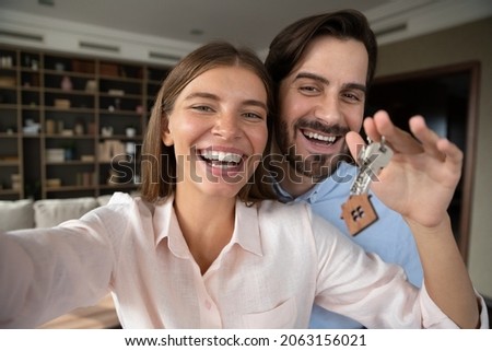 Happy emotional loving young family couple showing keys to camera, posing for selfie photo or recording video, feeling excited of moving into new renovated apartment, celebrating last mortgage payment