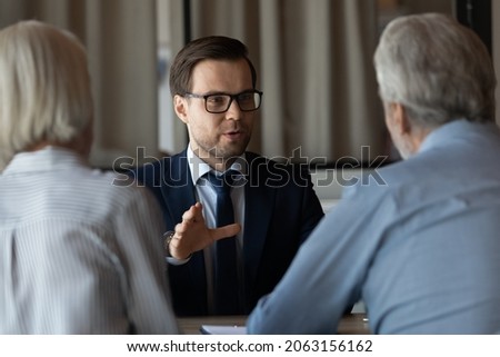Professional assistant. Confident young man financial advisor real estate agent talking consulting retired couple. Experienced businessman manager lawyer help clients aged spouses on meeting at office Royalty-Free Stock Photo #2063156162