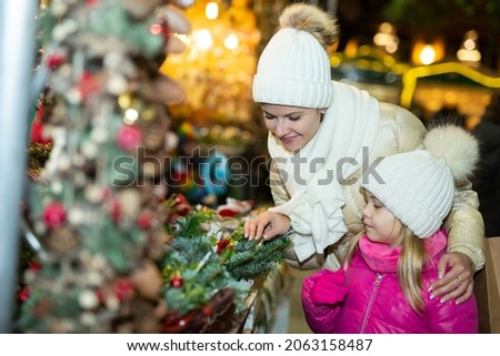 Cheerful little girl with mom choosing Christmas fairy lights at the street market. High quality photo