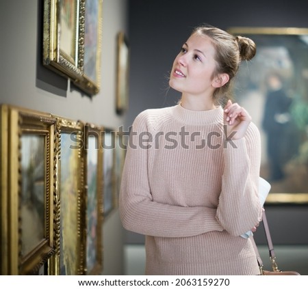 Portrait of young woman standing near the painting in the baguette in the art museum