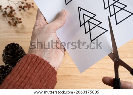 Close-up of hands cutting out paper Christmas ornament, wooden background, selective focus.