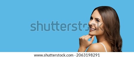 Portrait of looking up, cheerful smiling, thinking woman, isolated over bright blue color background. Brunette girl posing at studio. Wide composition with copy space free area for some text. Female.