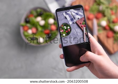 Man shooting fresh vegetable salad with mozzarella and spinach on cell phone camera. Cooking, blogging and healthy eating concept.