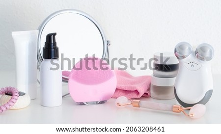 Cleanser and Microcurrent devices, Gua Sha roller, professional cleansing cloths , natural oil and serum, cream and masks on white table with mirror.Modern beauty routine banner