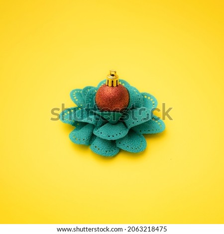 Red bauble on a green textile flower. Yellow background. Minimal