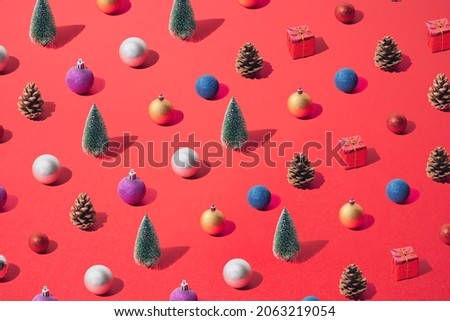 Arranged green New Year and Christmas tree with silver, yellow gold, blue, red, purple bauble, gift and brown cone on a red background. Pattern.