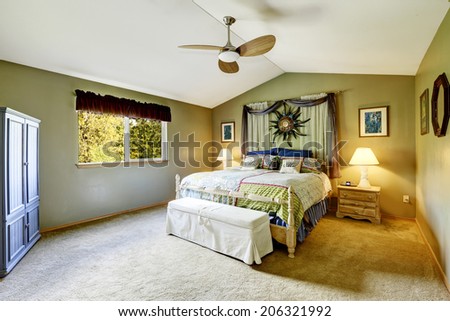 Spacious bedroom with vaulted ceiling. View of rustic bed with colorful bedding and curtains with wall art above it.