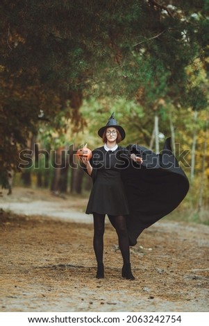 Halloween witch. Portrait of a girl in a hat and a witch costume with a pumpkin in the forest. Ready for the holiday "wallet or life"

