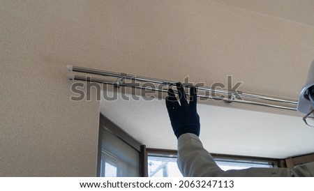 A worker inspecting a curtain rail in a room.