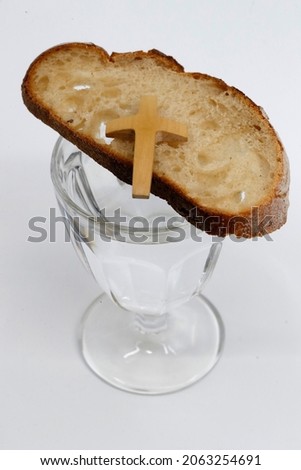 Lent starts on Ash Wednesday and ends on Holy Thursday Evening. Glass of water, christian cross and bread. France.  Royalty-Free Stock Photo #2063254691