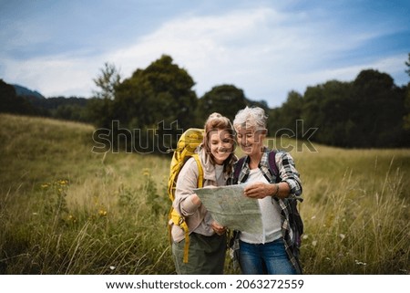 Happy mid adult woman with active senior mother hiking and looking at map outdoors in nature. Royalty-Free Stock Photo #2063272559