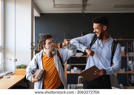 Young happy man with Down syndrome with his mentoring friend celebrating success indoors at school. Royalty-Free Stock Photo #2063272706