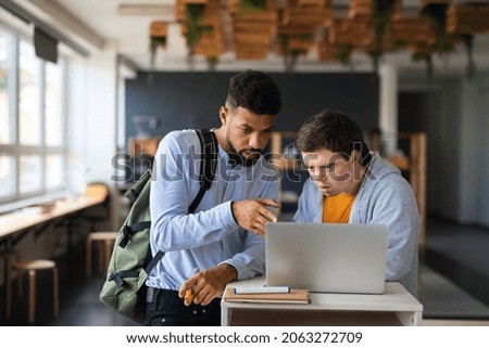 Happy young man with Down syndrome and his tutor using lapotp indoors at school. Royalty-Free Stock Photo #2063272709