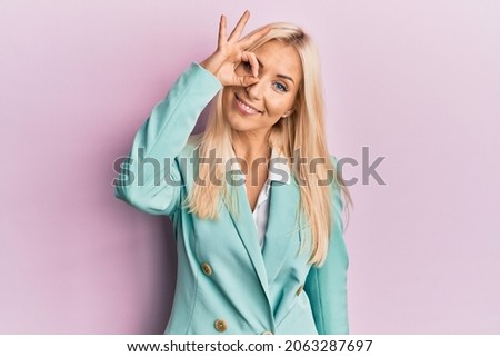 Young blonde woman wearing business clothes smiling happy doing ok sign with hand on eye looking through fingers 