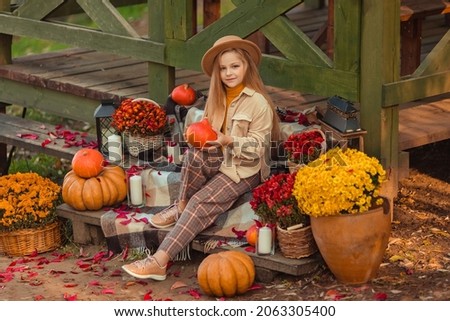 girl in a hat with autumn decor with pumpkins and flowers