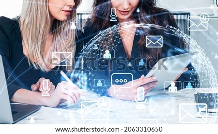 Young attractive businesswoman wearing formal suit is talking to colleague. Office workplace in the background. Digital interface with hologram of virtual globe in the foreground. Concept of teamwork