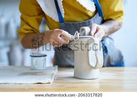 Craftswoman at work using tools for scraping and shaping clay jug in art studio. Closeup of ceramics master preparing pottery jag. Art hobby for recreation and small business in craft store concept