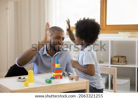 Happy young african american father giving high five to joyful little child son, playing toys together at home. Emotional joyful mixed race two male generations family entertaining on weekend. Royalty-Free Stock Photo #2063321255