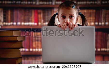 Education concept. Portrait of young beautiful child girl working  with laptop and reading books in library. Horizontal image. Copy space.