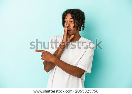 Young african american man isolated on blue background saying a gossip, pointing to side reporting something.