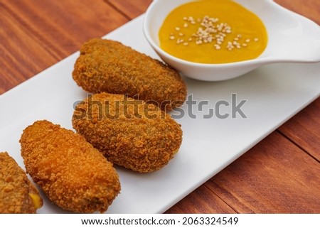 Fried croquettes with yellow sauce on white plate. Side view on wooden background.