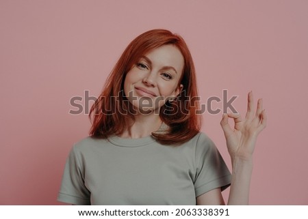 Body language concept. Calm satisfied redhead female showing OK sign, making okay gesture with fingers while posing isolated over pink studio background, smiling woman giving her approval