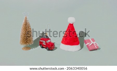 Gray background with Christmas or New Year symbol attribute objects and symbolic items concept. Pink gift box present with ribbon, small red taxi car toy, fir tree and red festive santa hap or cap