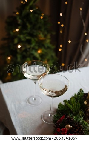 Two glasses of champagne with lights in the background. Nearby there are decorations and a wreath of greenery. Shallow depth of field for atmospheric photography. Holiday concept New Year 2022.