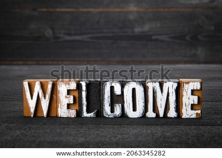 Welcome. White wooden letters on a dark wooden background.