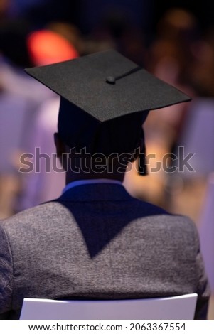 Sharp shadow silhouette of alumnus graduation square academic cap including tassel against an out of focus blurred colorful ceremonial background
