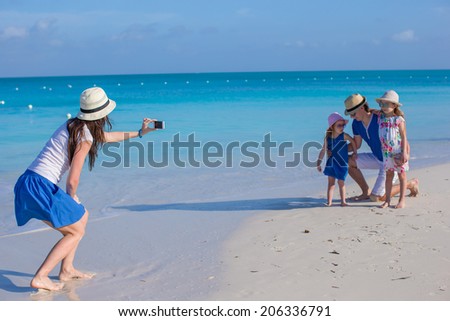Young mother making photo on phone of her family at the beach