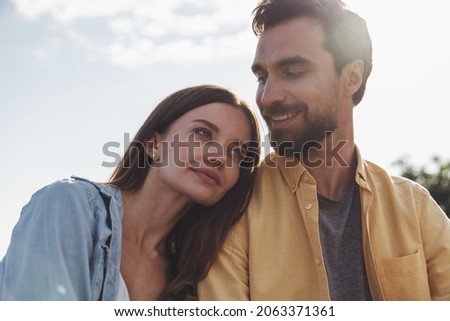 Portrait of young happy couple, girl holding head on boy's shoulder on sunny sky background.