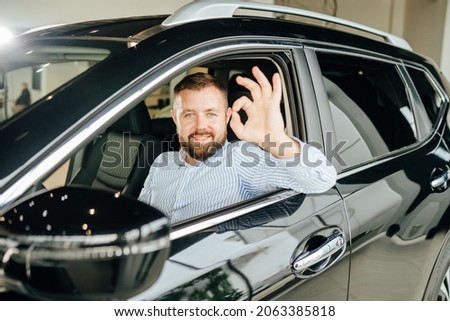Happy male owner of new crossover auto gesturing sign ok on camera. Caucasian man sitting inside modern car and feeling happiness from expensive purchase.