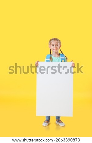 Cute little schoolgirl with blank poster on color background