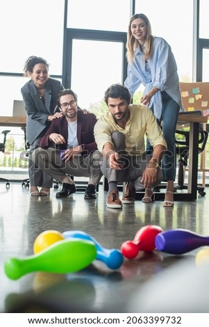 Businessman playing bowling near smiling interracial colleagues in office